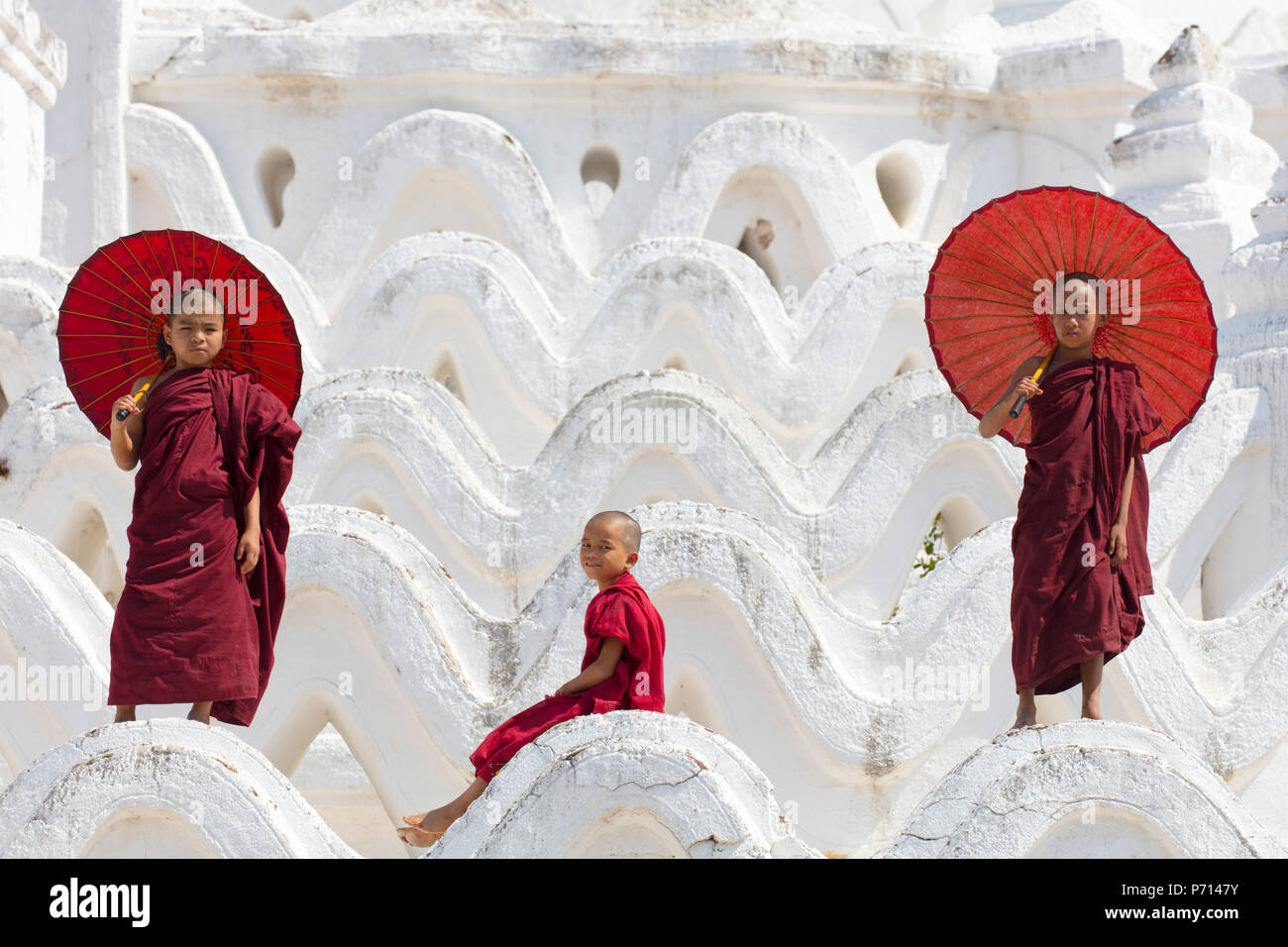 Drei junge Mönche in rot gekleidet, mit roten Sonnenschirme am Myatheindan Pagode (weiße Tempel) in Mingun, Myanmar (Burma), Asien Stockfoto