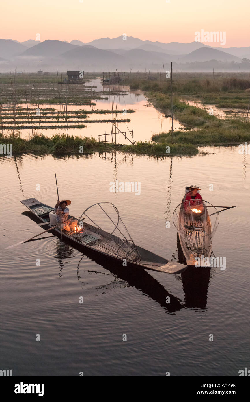 Zwei Fischer warm halten in ihren langen Schwanz Fischerboote in der Dämmerung in der Nähe der schwimmenden Gärten am Inle See, Shan Staat. Myanmar (Burma), Asien Stockfoto