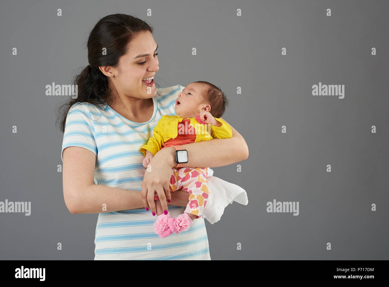 Lachende junge Hispanic Mutter mit Baby girl portrait auf grauem Hintergrund Stockfoto