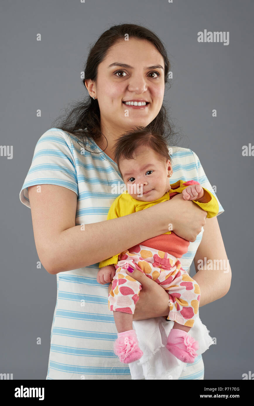Portrait von Happy hispanic Mutter mit Baby auf grauem Hintergrund Stockfoto