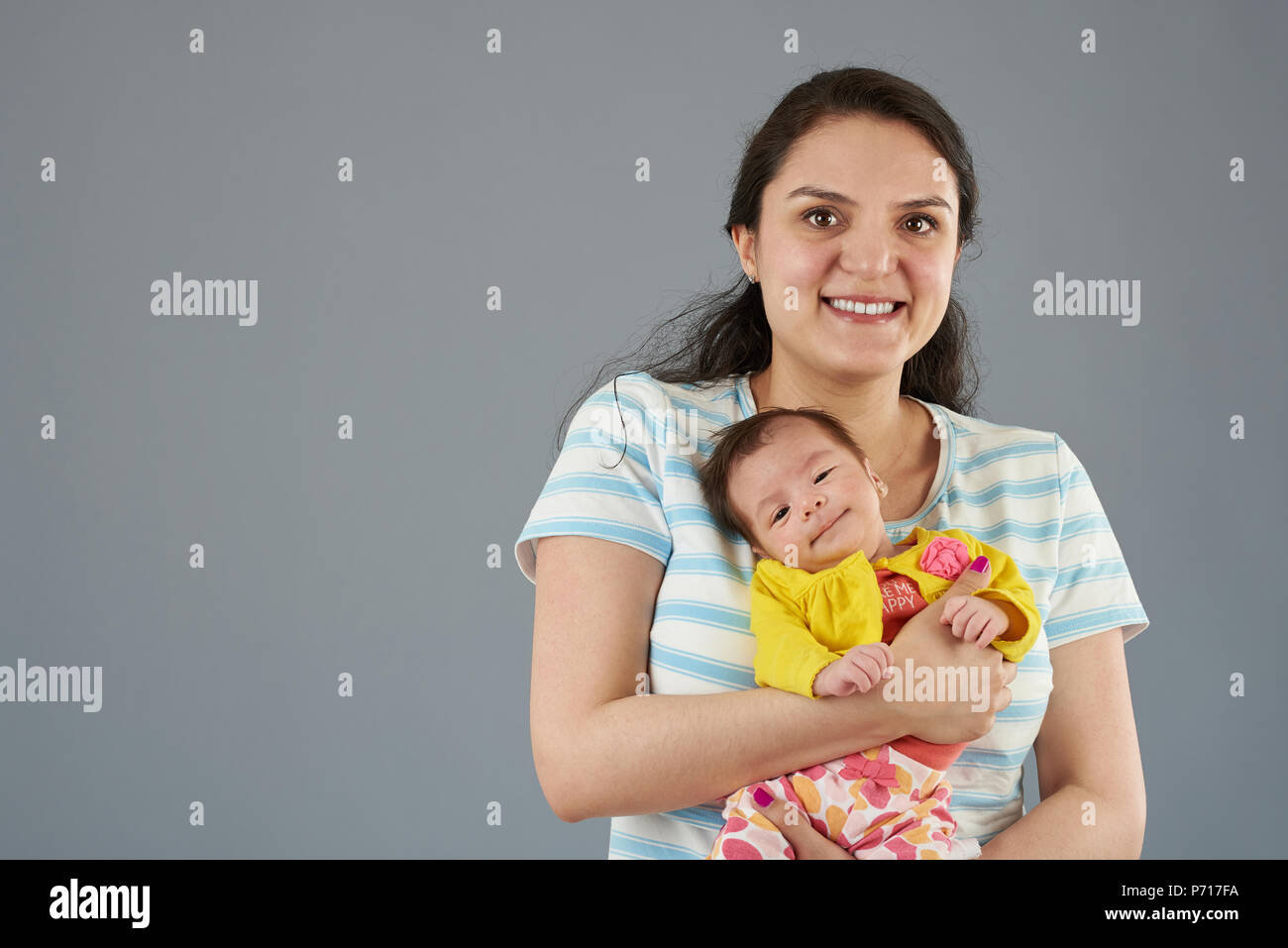 Junge hispanic Mutter mit kleinen niedlichen Baby Mädchen auf grauem Hintergrund portrait isoliert Stockfoto