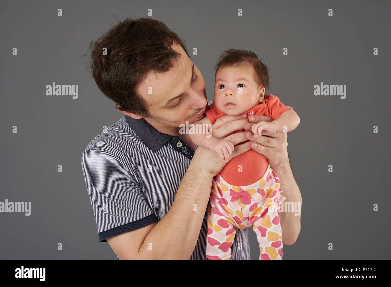 Cute Baby in Vaters Hände auf grauem Hintergrund Stockfoto