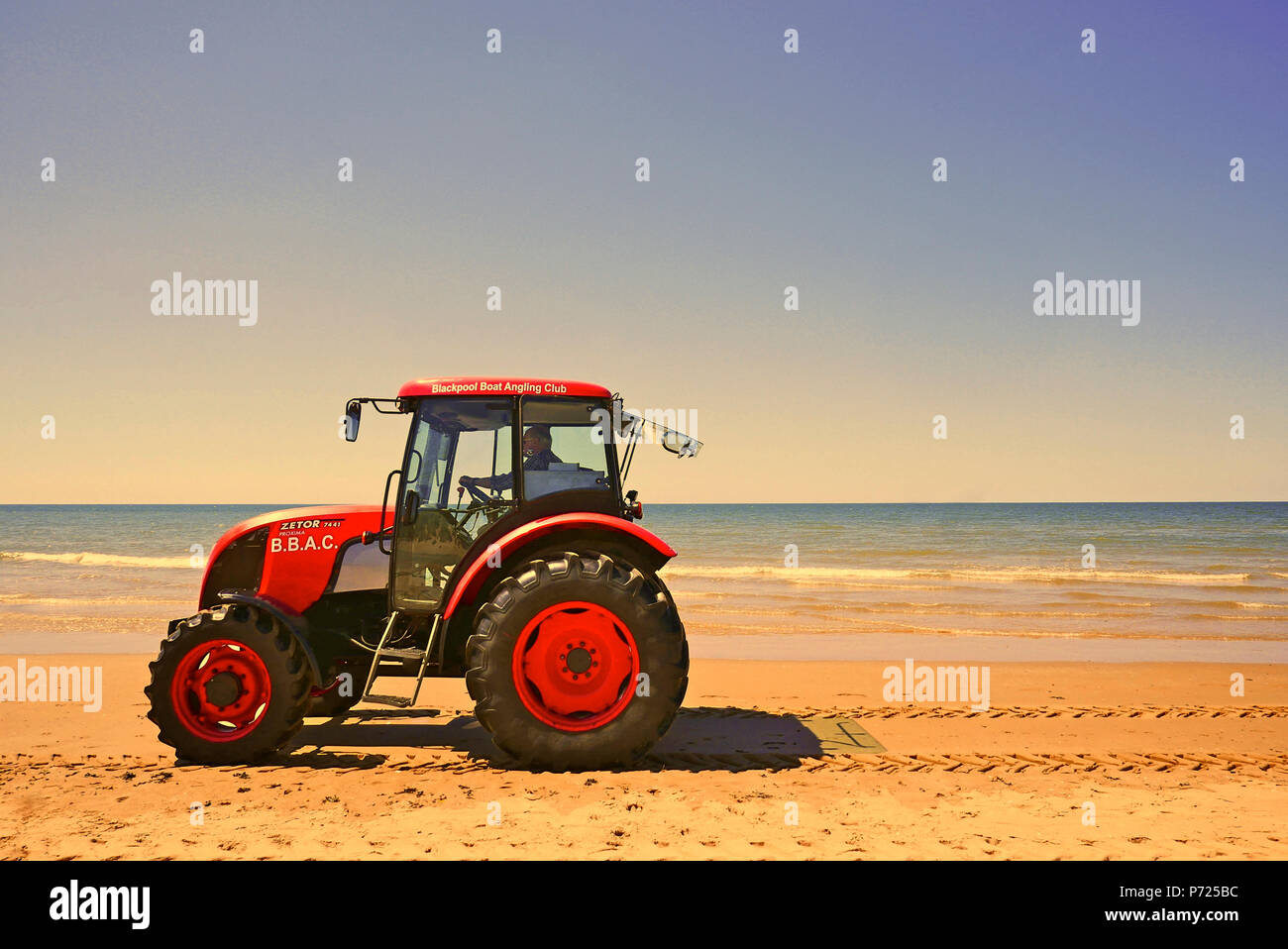 Roter Traktor am Strand gegen den blauen Himmel und Meer Stockfoto