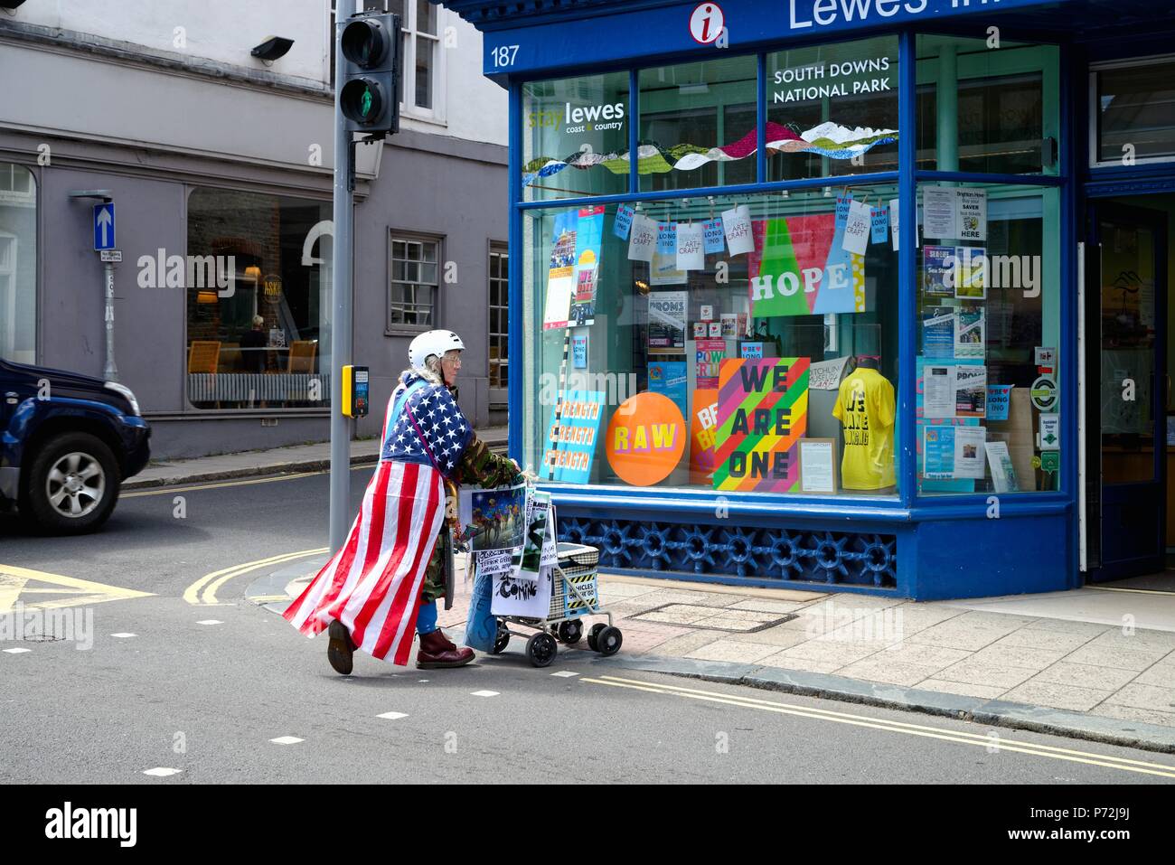 Eine ältere Frau trägt einen Helm und das amerikanische Sternenbanner Flagge treibt ein Trolley mit Protest Plakate in Lewes High Street UK Stockfoto