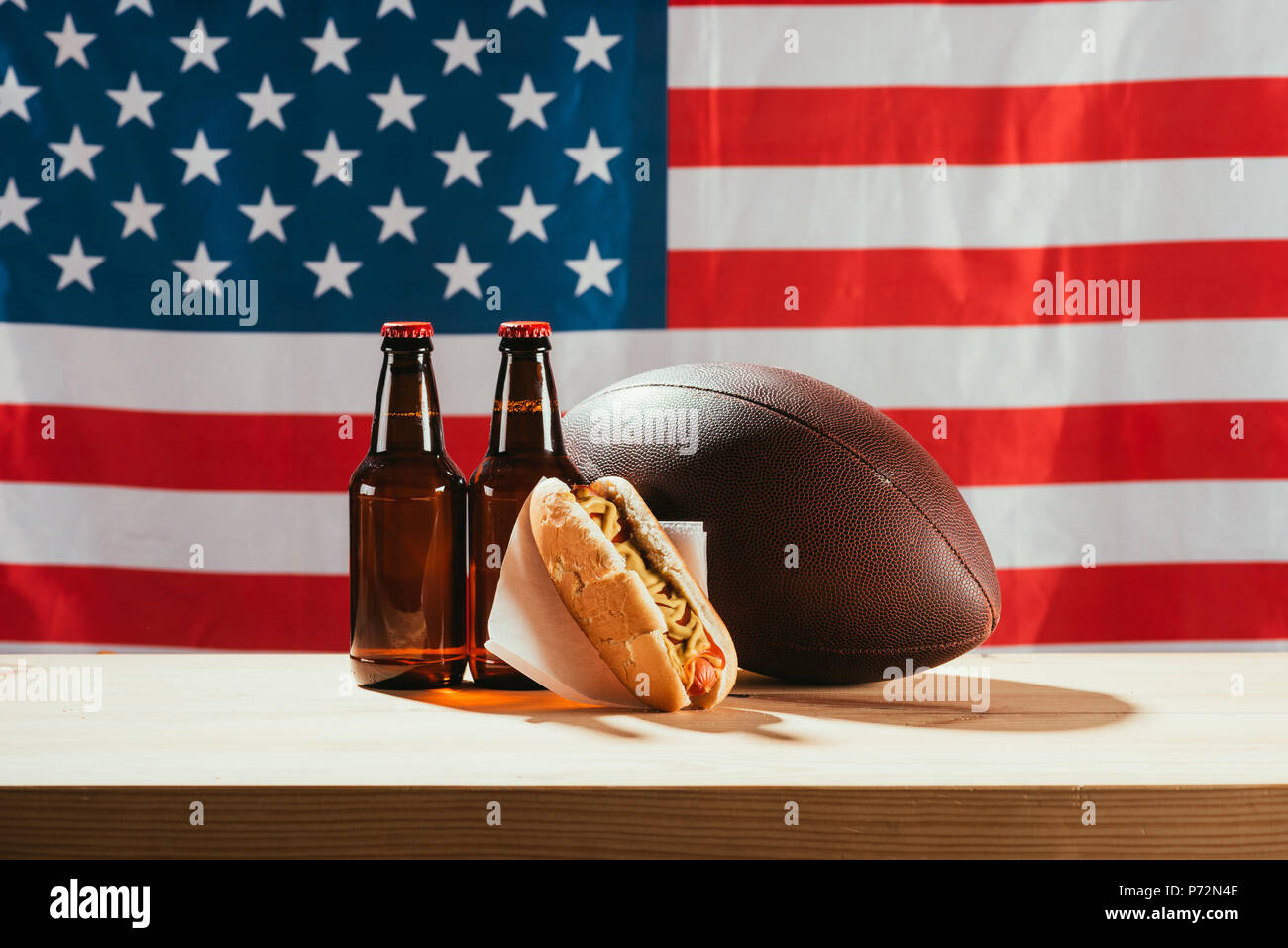 Nahaufnahme der Bierflaschen, Hot Dog und Rugby Ball auf Holztisch mit us Flag hinter Stockfoto