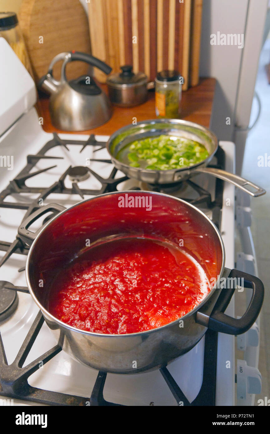 Kochen einen Topf mit roter Tomatensoße und eine Pfanne mit Paprika auf einem Gasherd und ein Glas heißen grüne chiles Küche, Kochen, Essen, Abendessen, Topf, Tomat Stockfoto