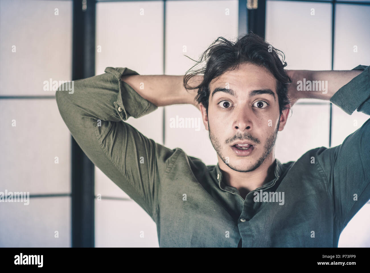 Ein hübscher junger Mann, 20 Y, posiert im Studio das Berühren des Kopfes. Angst Ausdruck. Green Rock. Retroilluminated stände im Hintergrund. Stockfoto