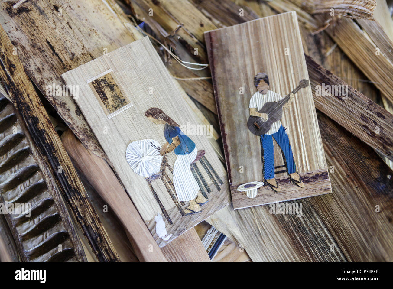 Florianópolis, Santa Catarina, Brasilien. Nahaufnahme von Bilder mit Mann spielt Gitarre und Frau Sticken mit Stroh und Holz. Stockfoto