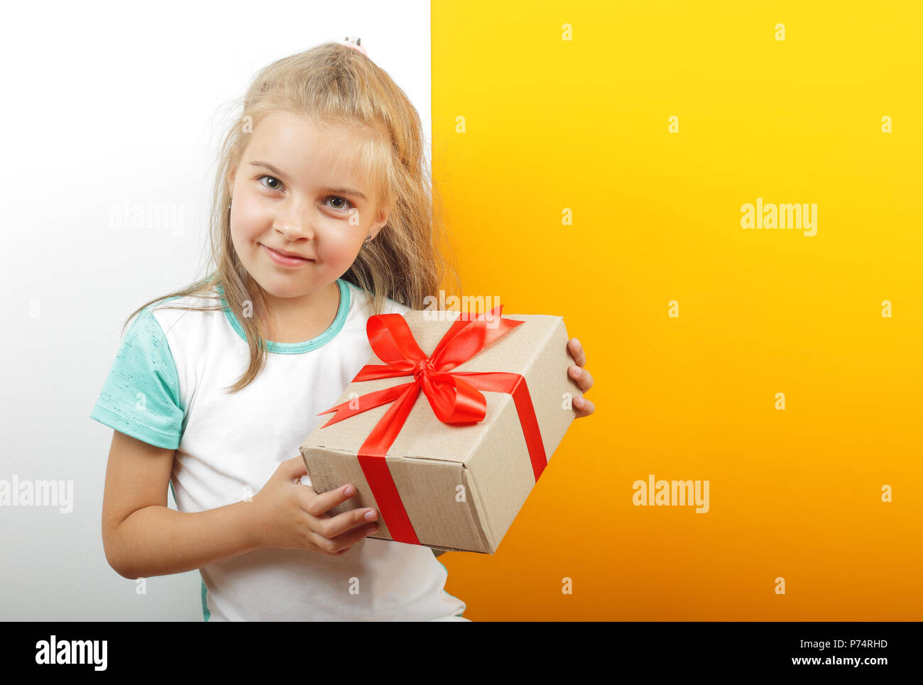 Geschenke, Shopping und präsentieren - Geschenkbox ist in den Händen des Mädchens auf einem gelben und weißen Hintergrund gebunden. Stockfoto