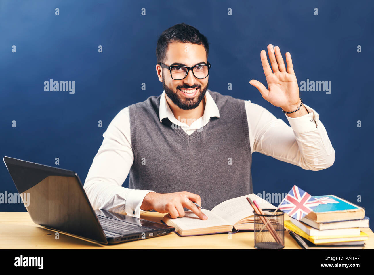 Dunkelhaarige bärtiger Mann Englisch lernen, tragen graue Strickjacke Weste und unberührten, weißen Hemd, die Hand vor der schwarzen Wand Stockfoto