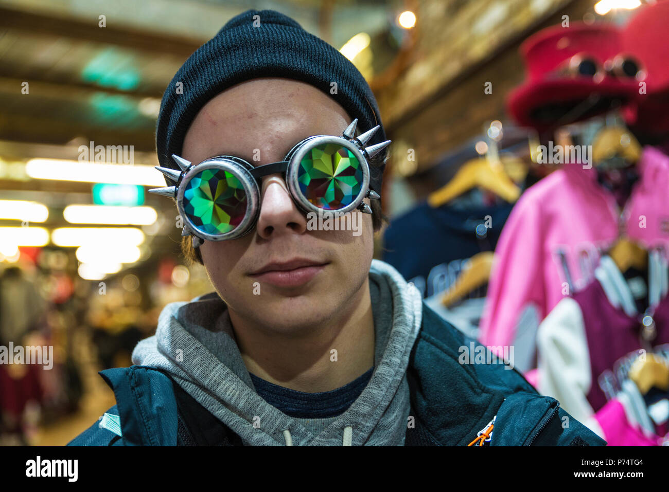 Teenager Junge mit einem gotischen Sonnenbrille mit gebeugten Objektiv oder Kaleidoskop in einem Fashion Shop der Camden Lock Market oder Camden Town in London, England, Stockfoto