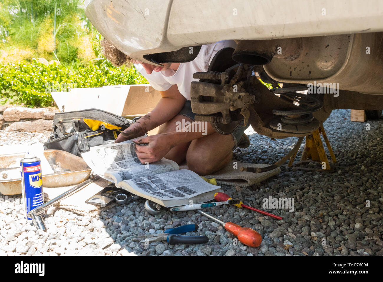 Heimwerker Auto Wartung und Reparaturen - junger Mann lesen Haynes manual, als er Änderungen der Bremsbeläge, Bremsscheibe und Bremssattel zum ersten Mal Stockfoto