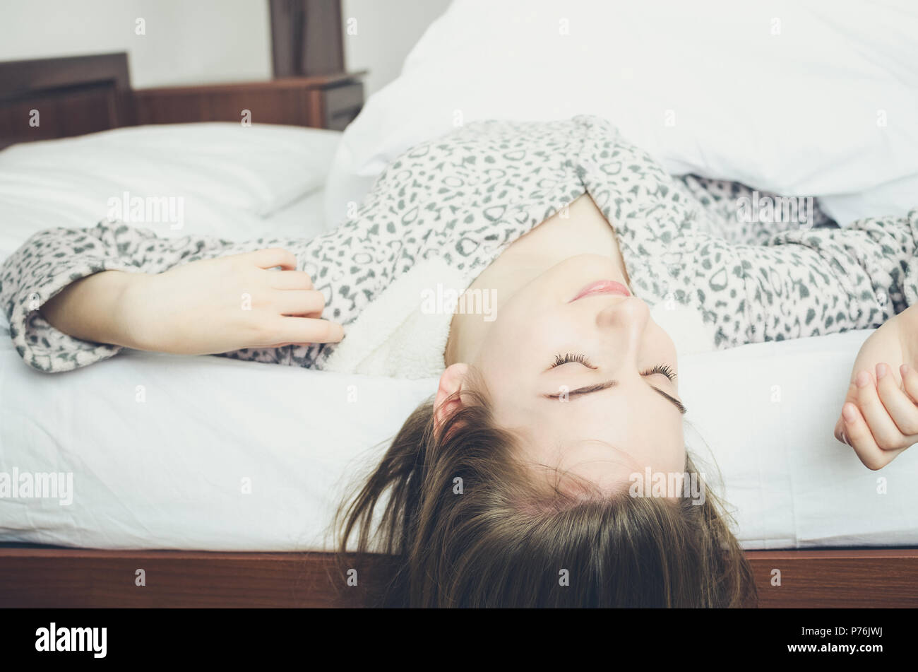 Glückliche junge Frau genießt sonnigen Morgen. Kaukasische Mädchen in süßen warme Schlafanzüge Stretching im Bett und lächelnd nach dem Aufwachen. Guter Start in den Tag Stockfoto
