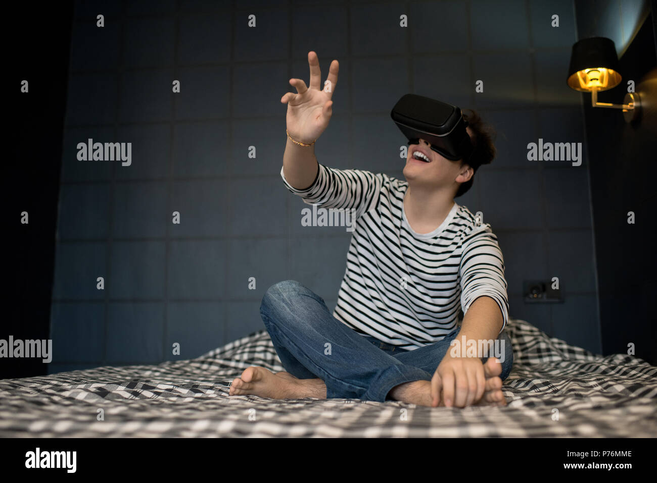 Junger Mann hand Verlängerung bei der Verwendung von Virtual reality Headset sitzen auf Bett im dunklen Zimmer begeistert. Stockfoto