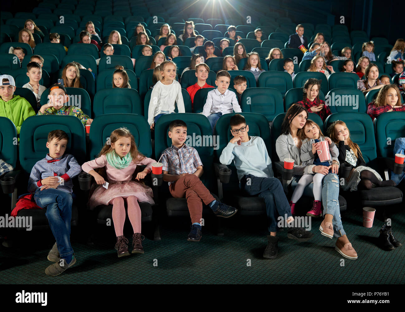 Von vorne: viele Kinder und Jugendliche im Kino sitzen und Cartoon genießen. Süße kleine Mädchen sitzen auf ihrer Mutter runden. Zuschauer expre Stockfoto