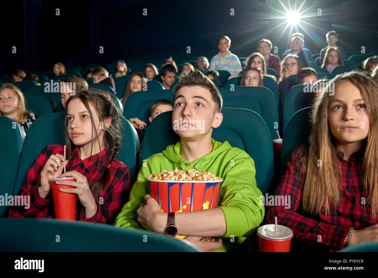 Junge Freunde ansehen Film mit unerschütterlichem Augen und sitzt im Kino und schaut mit Interesse auf dem Bildschirm. Jugendliche trinken kohlensäurehaltige Getränke und Essen Stockfoto