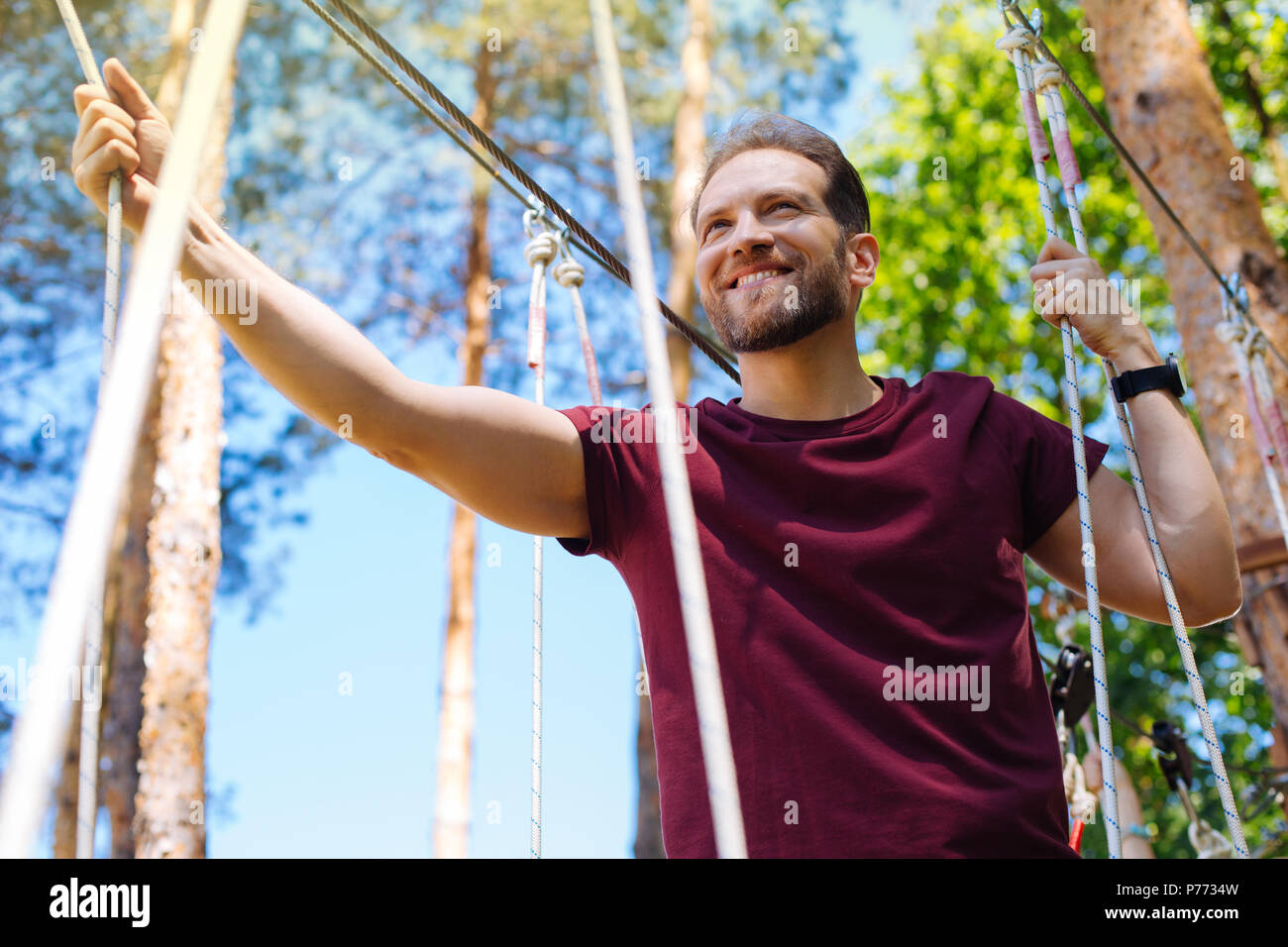 Fröhlicher junger Mann Klettern in einem Hochseilgarten Stockfoto