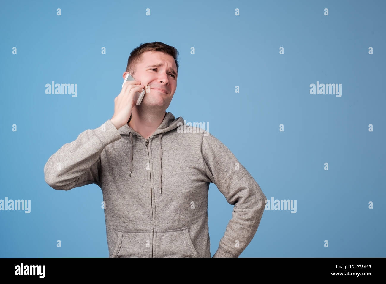 Attraktiven europäischen Mann recieving unangenehme Nachricht oder Anruf auf blauen Hintergrund irritiert. Stockfoto