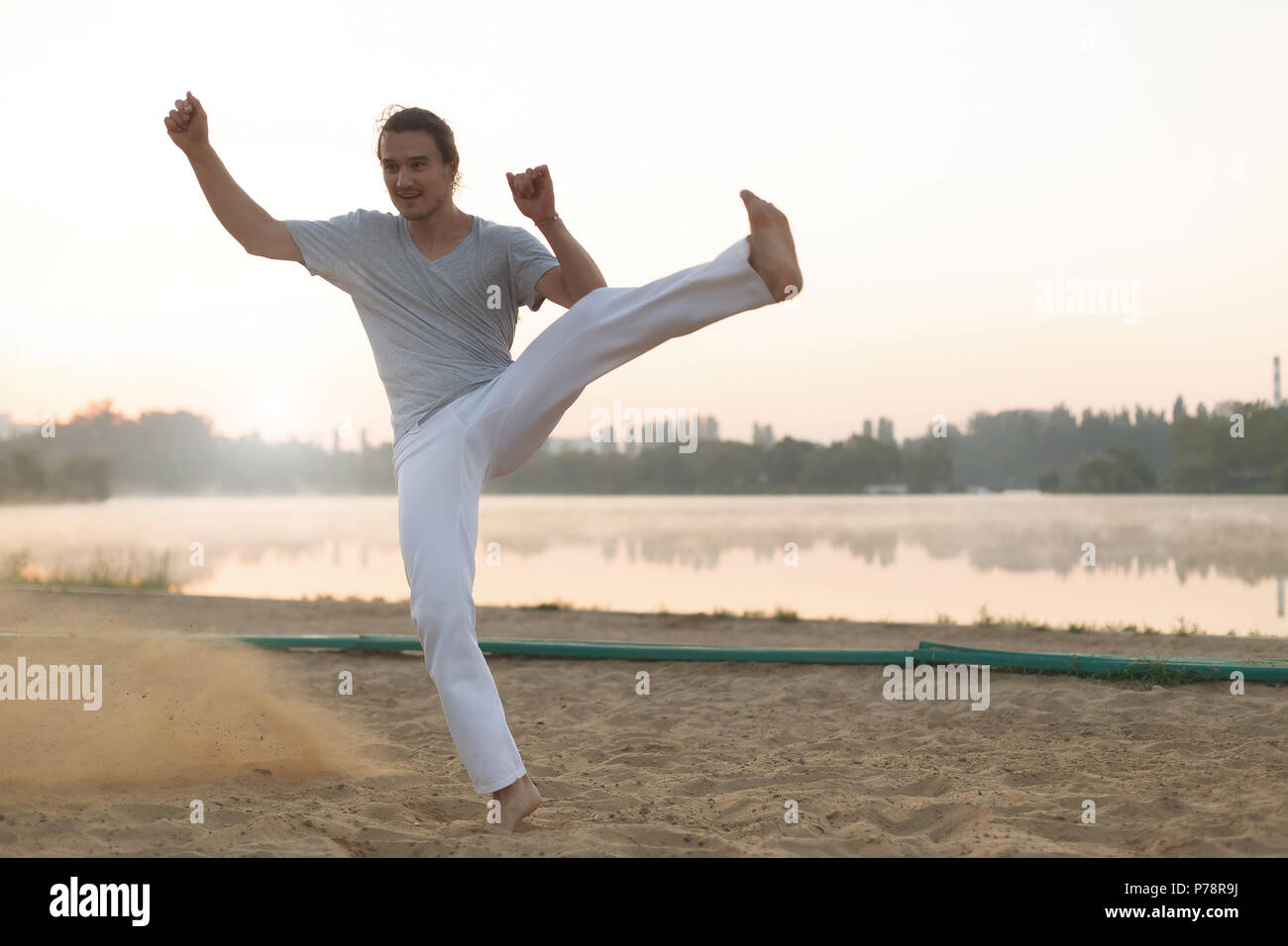 Konzept über Leute, Lifestyle und Sport. Capoeira am Strand, in der Nähe der See im Park ein Performer, bei Sonnenaufgang. Casual athletischen Mann im weißen Hosen, Stockfoto
