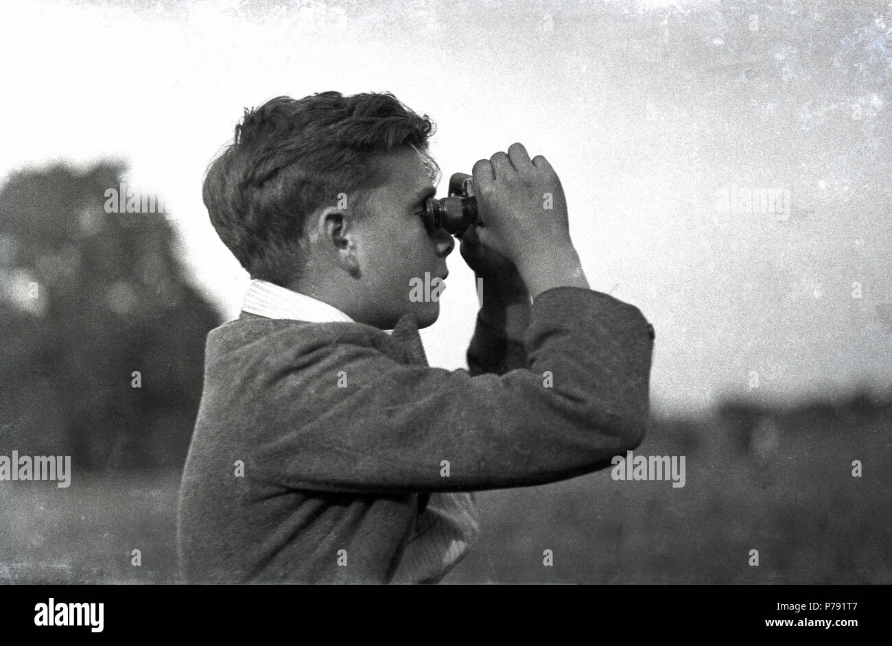 1930er Jahre, historische Bild eines Schülers draußen zu sitzen mit einem Fernglas tp anzeigen oder etwas in der Ferne, England, UK. Stockfoto