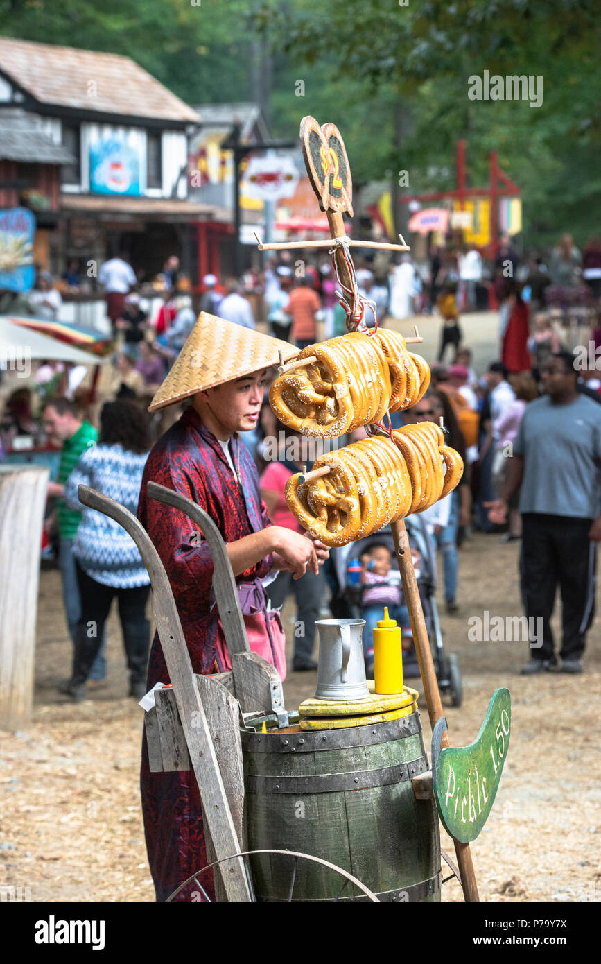 Orientalische Brezel Verkäufer trägt einen konischen Chillba hat verkauft, um ihre Waren im Freien an einem sonnigen Tag am Maryland Renaissance Festival. Essiggurken zum Verkauf. Stockfoto