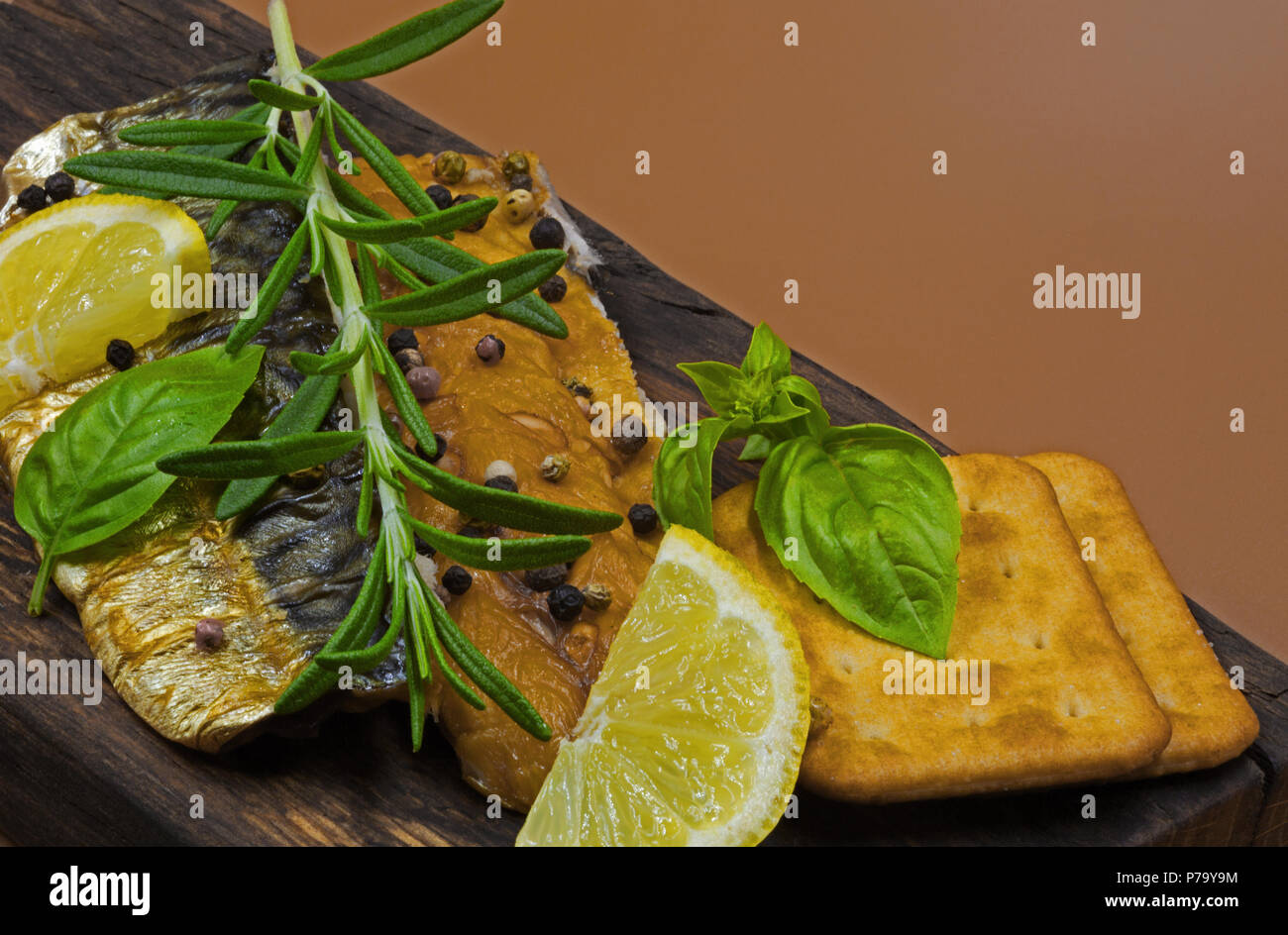 Zwei Stücke von geräucherter Makrele bestreut mit bunten Pfeffer, mit Zitrone garniert, einen frischen Zweig Rosmarin und Basilikum, auf einer alten Holz- Board Stockfoto