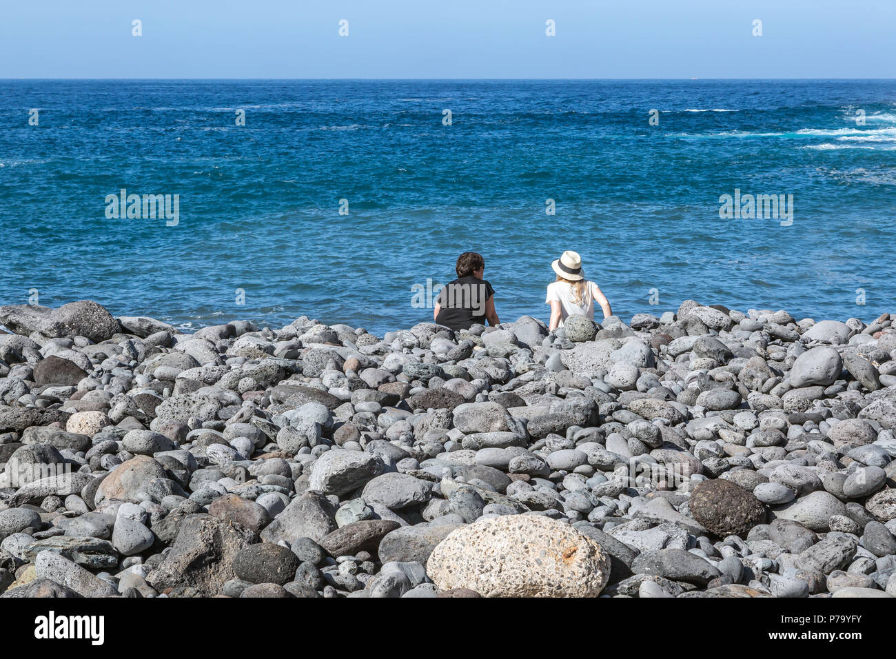 Eine Ansicht von hinten von einer Mutter und Tochter sitzen auf einem Kieselstrand in Richtung der Nördlichen Atlantik suchen. Teneriffa, Kanarische Inseln. Stockfoto