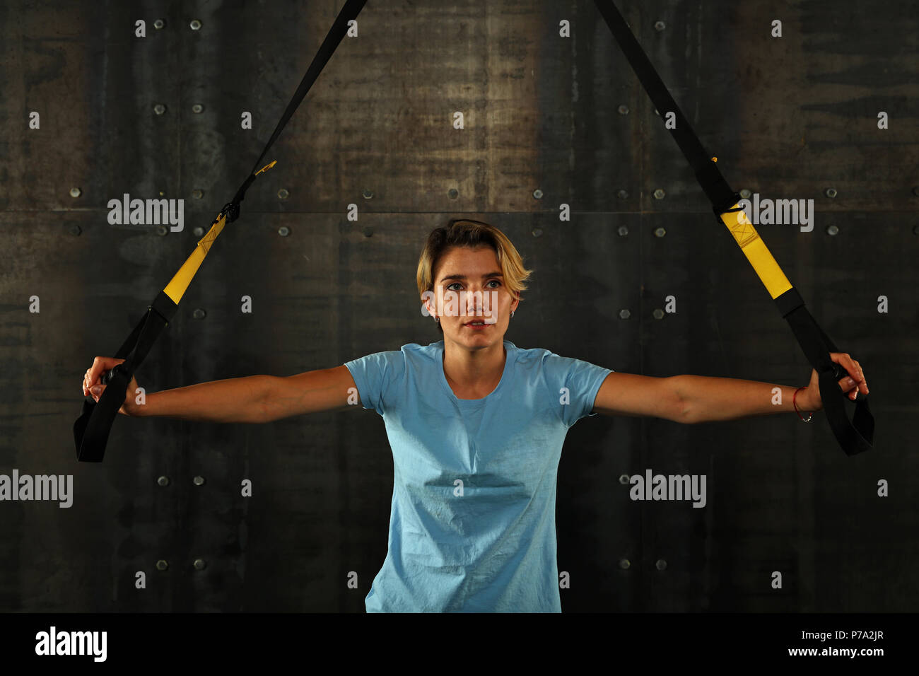 Eine junge athletische Frau bei crossfit Schulung, Training mit TRX Suspension fitness Bänder über dunklen Hintergrund, Vorderansicht, von der Kamera suchen Stockfoto