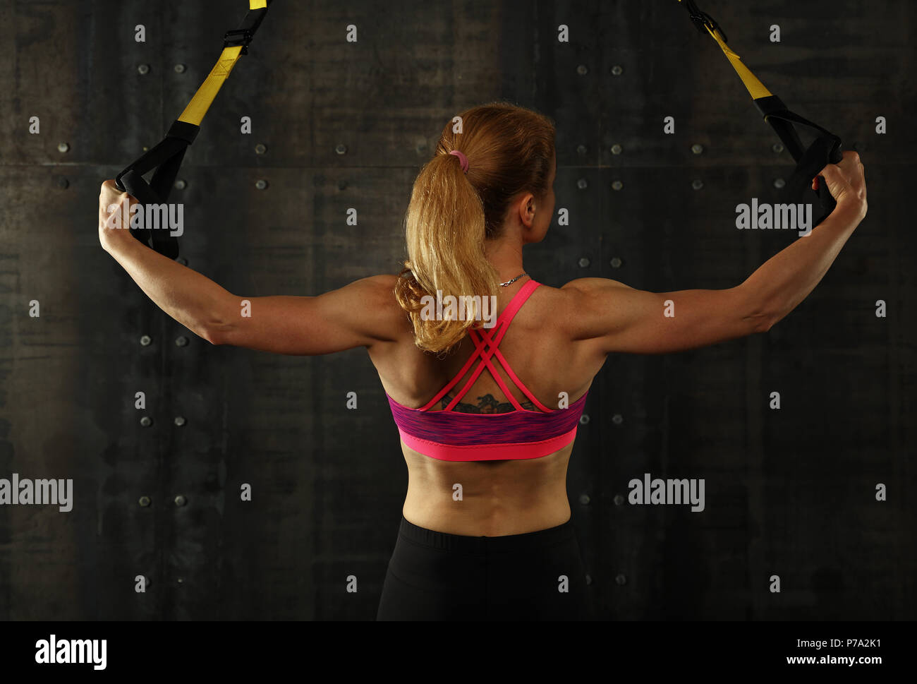 Ansicht der Rückseite Porträt einer jungen und mittleren Alter athletische Frau bei crossfit Schulung, Training mit TRX Suspension fitness Bänder über dunklen Hintergrund Stockfoto