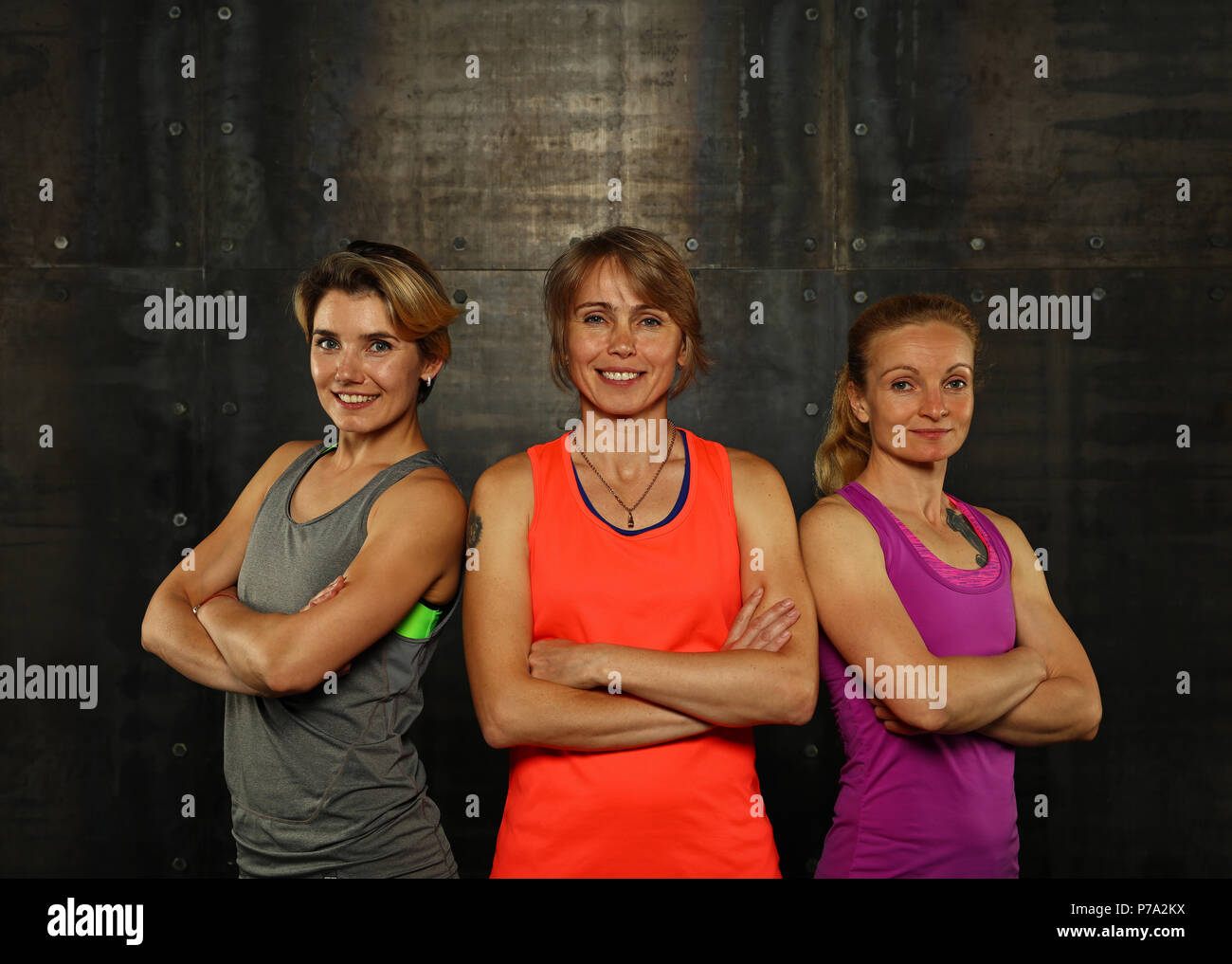 Schließen Sie herauf Frontseite Portrait von drei jungen und mittleren Alters athletische Frauen in Sportkleidung in der Turnhalle über der dunkle Hintergrund, bei Camera suchen Stockfoto