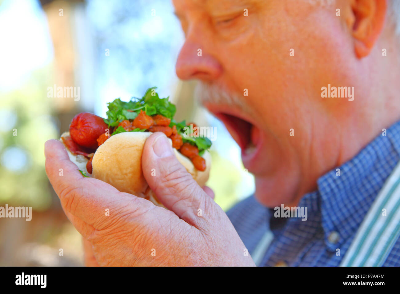 Mann essen einen Hot Dog mit Chili Bohnen und gehackt Salat Stockfoto