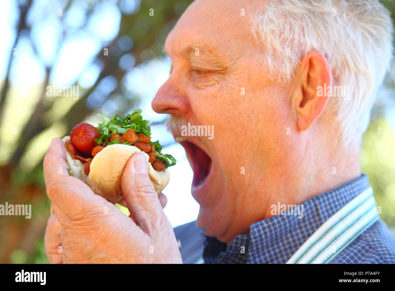 Mann mit Schürze bereit, in einen Hot Dog mit Chili zu beißen und gehackt Salat Stockfoto