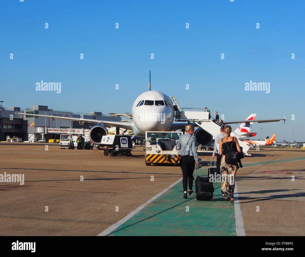 Zwei weibliche Passagiere gehen Sie in Richtung Thomas Cook Airlines Airbus 321 Hand ziehen Gepäck hinter Ihnen. Stockfoto