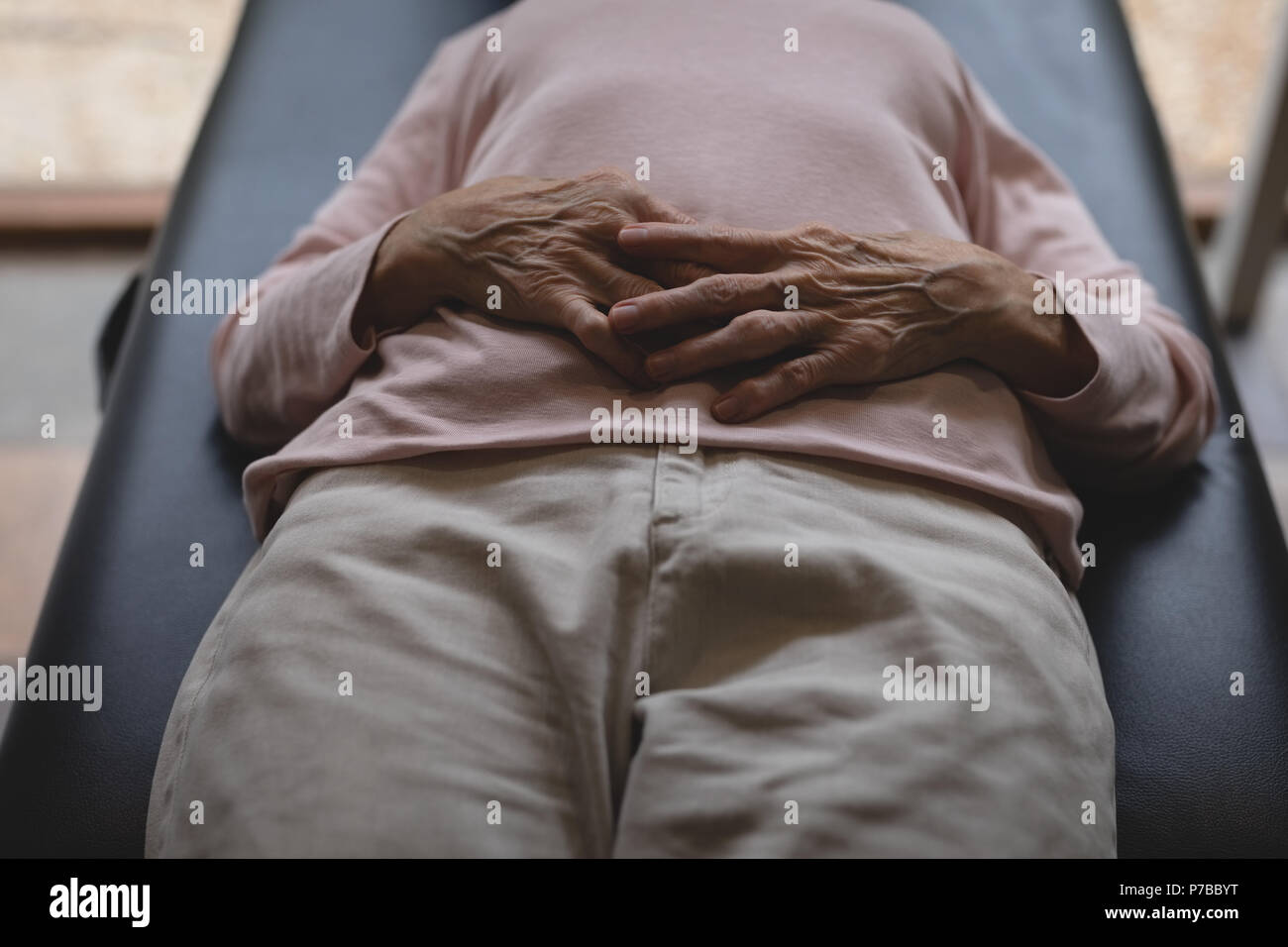 Ältere Frau liegend auf Bett mit Hand auf Magen Stockfoto