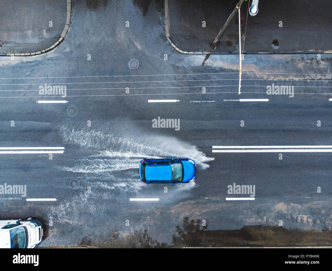 Blaues Auto auf nasser Straße nach starkem Regen. Spritzer und Pfützen auf der Straße überschwemmt. Luftaufnahme Stockfoto