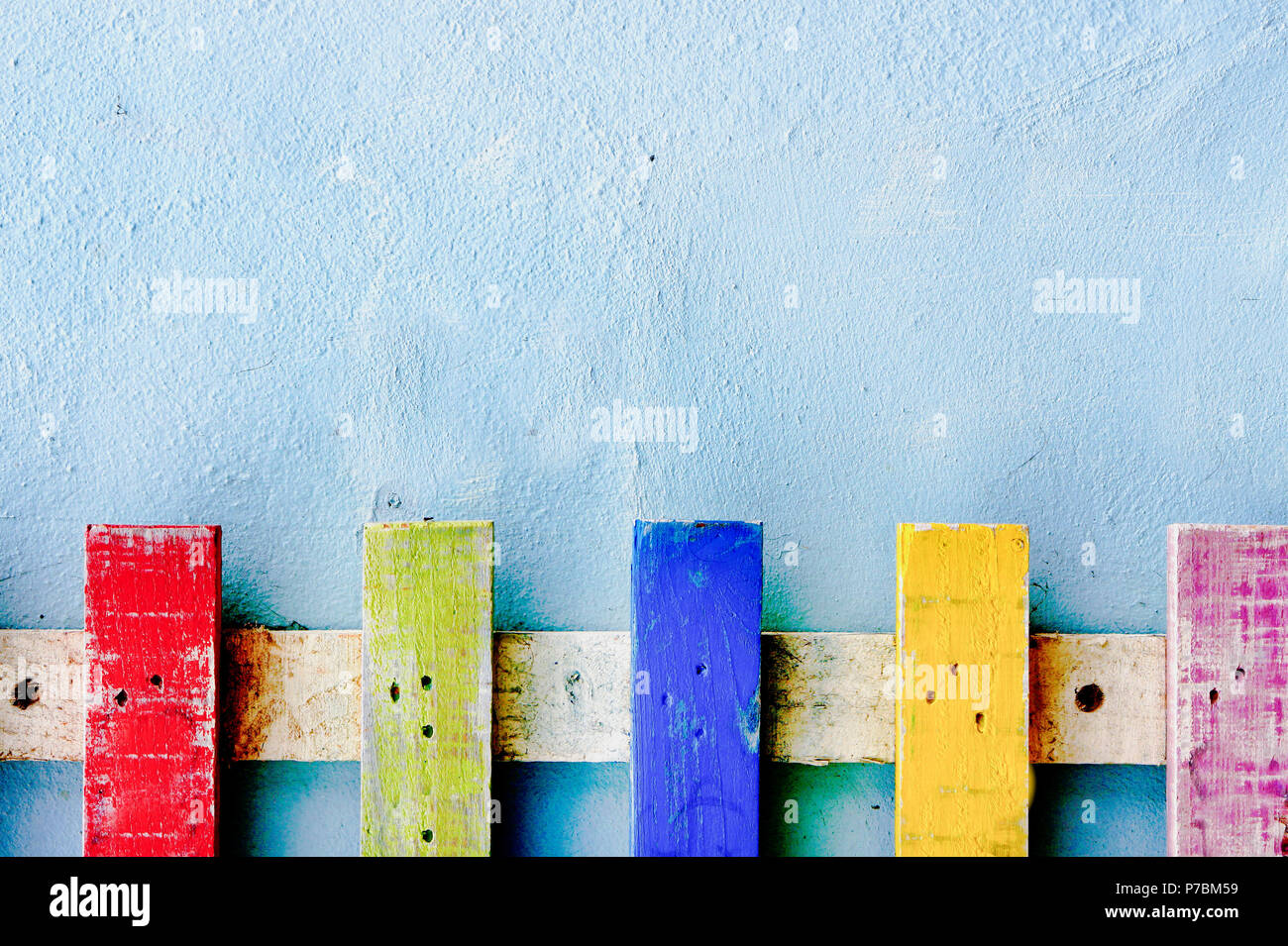 Teil eines bunten Lattenzaun vor einem blauen Stein Wand Stockfoto