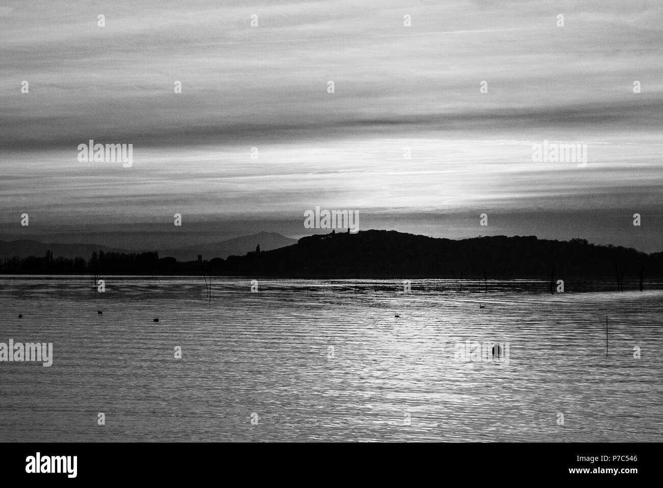 Lago Trasimeno (Umbrien) in der Dämmerung, mit sanften Farbtönen in den Himmel und Wasser, Lichtreflexe und Vögel auf dem Wasser Stockfoto