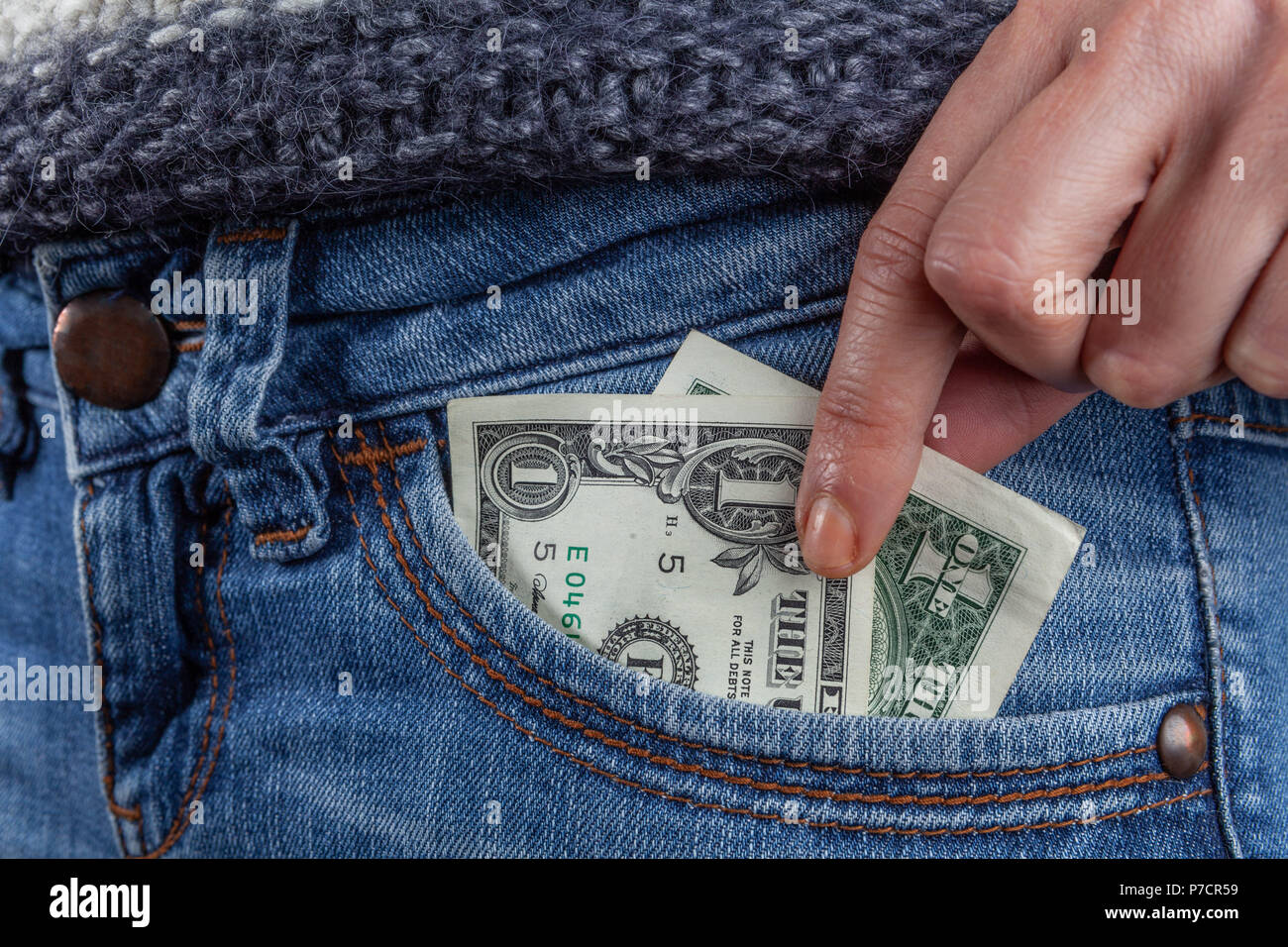 Weibliche Hand erreichen für 1 Dollar Bill in Blue Jeans Tasche vorne closeup - Mindestlohn und schlechte Wirtschaft Konzept Stockfoto
