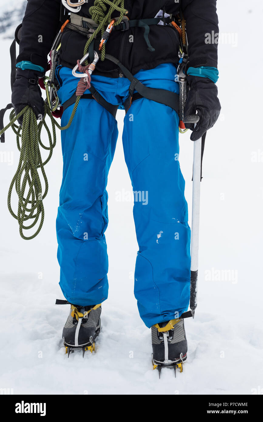 Männliche Bergsteiger stehend mit Seil und Eispickel an einem verschneiten Region Stockfoto