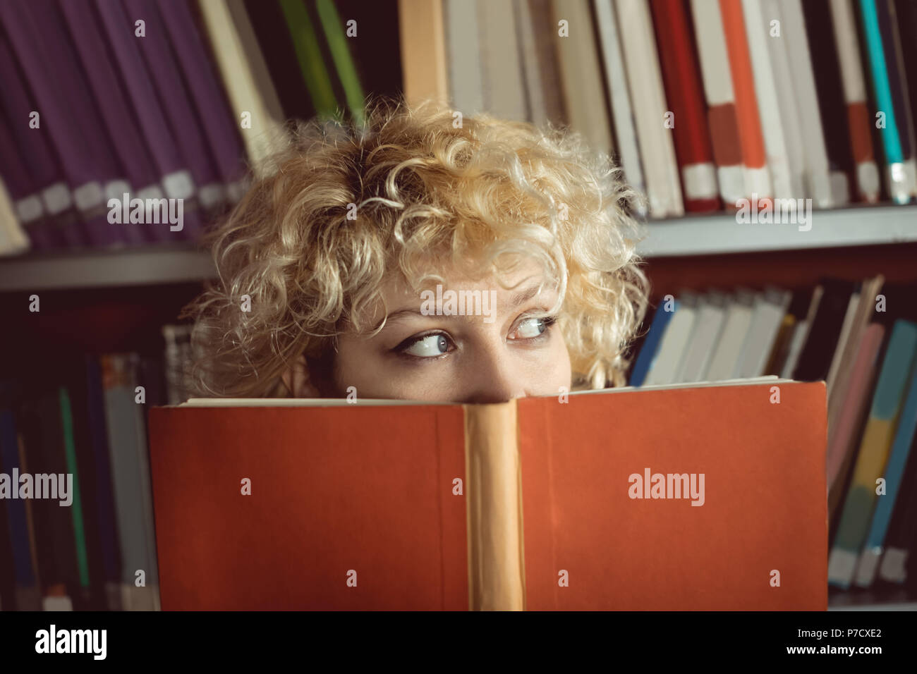 Frau verbergen ihr Gesicht hinter Buch in der Bibliothek Stockfoto