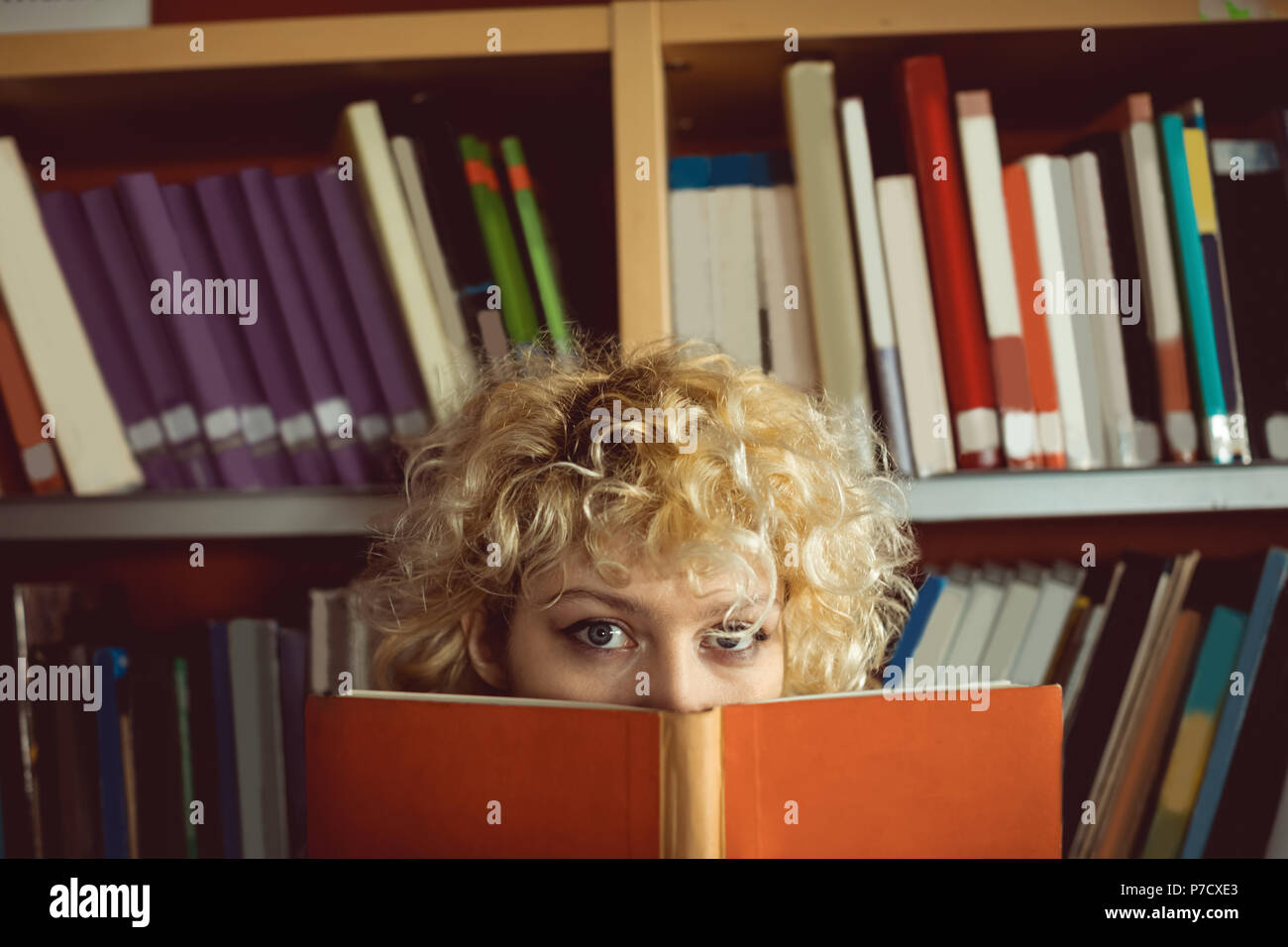 Junge Frau ihr Gesicht verstecken hinter Buch in der Bibliothek Stockfoto