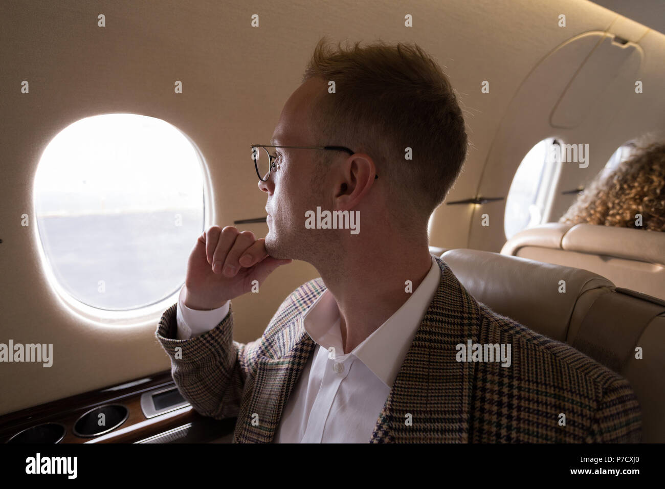Geschäftsmann auf der Suche durch das Fenster während der Fahrt im privaten Jet Stockfoto