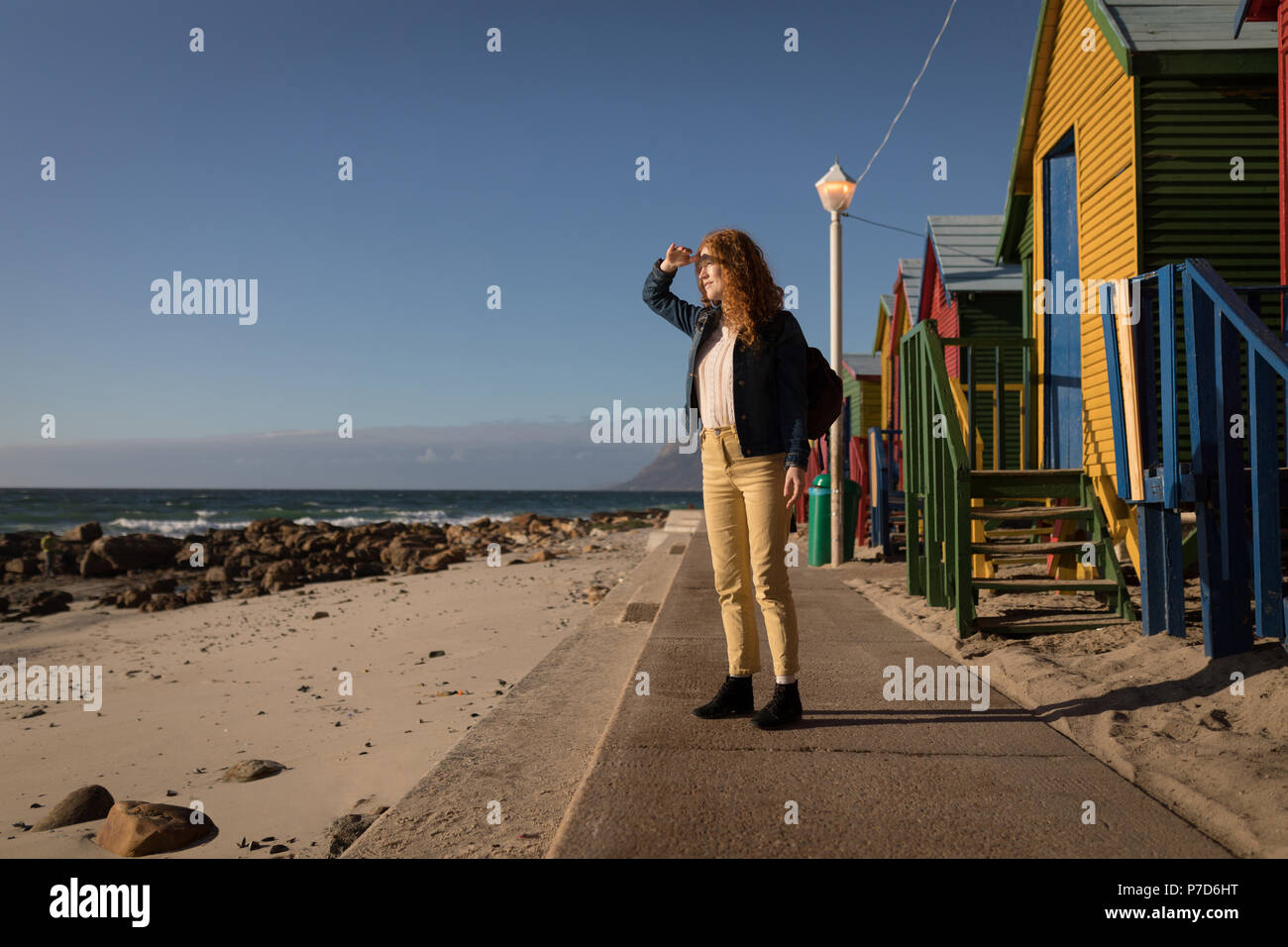 Frau Abschirmung ihre Augen in der Nähe der Umkleidekabinen am Strand Stockfoto
