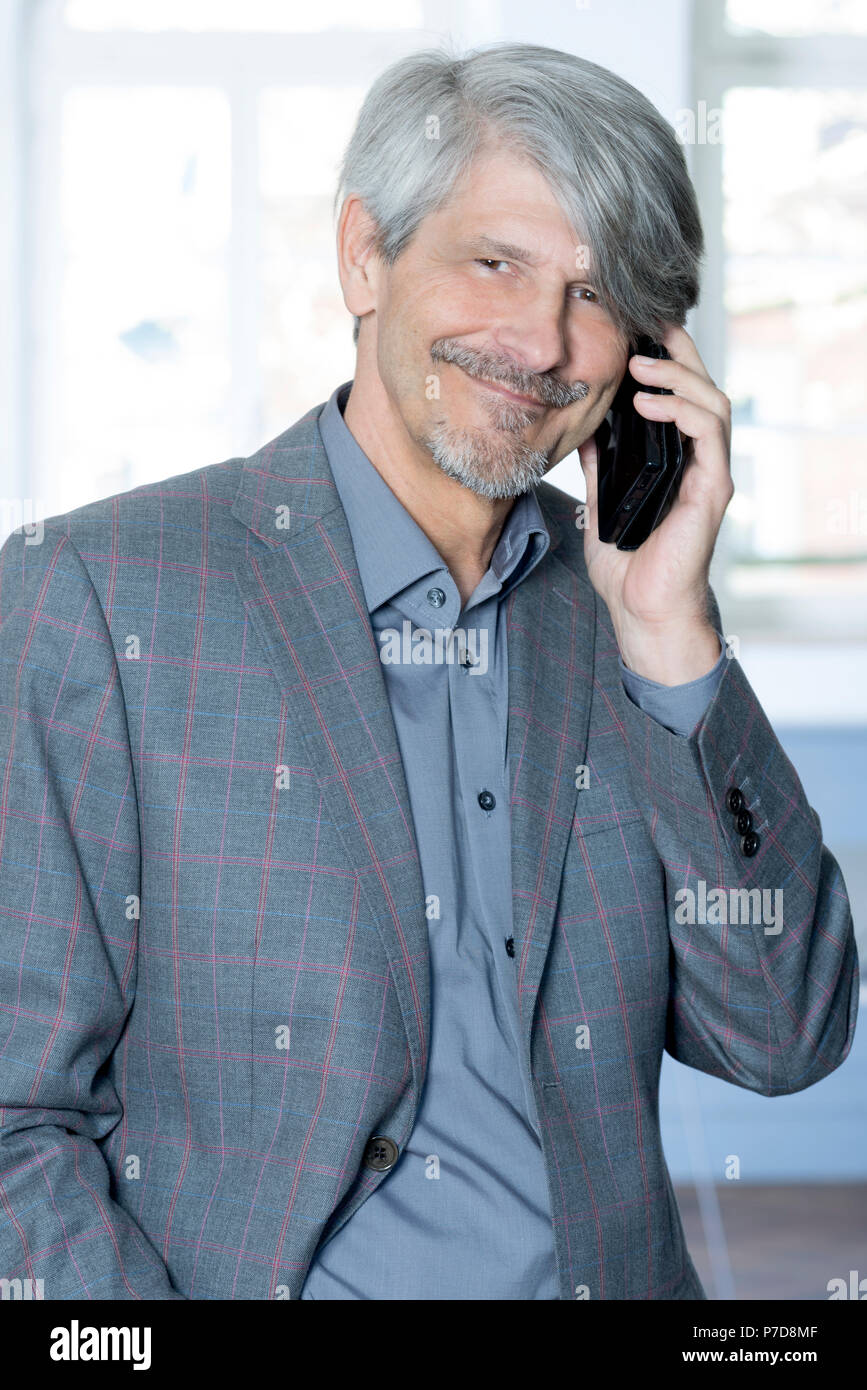 Mann mit Handy vor seinem Bürofenster Stockfoto