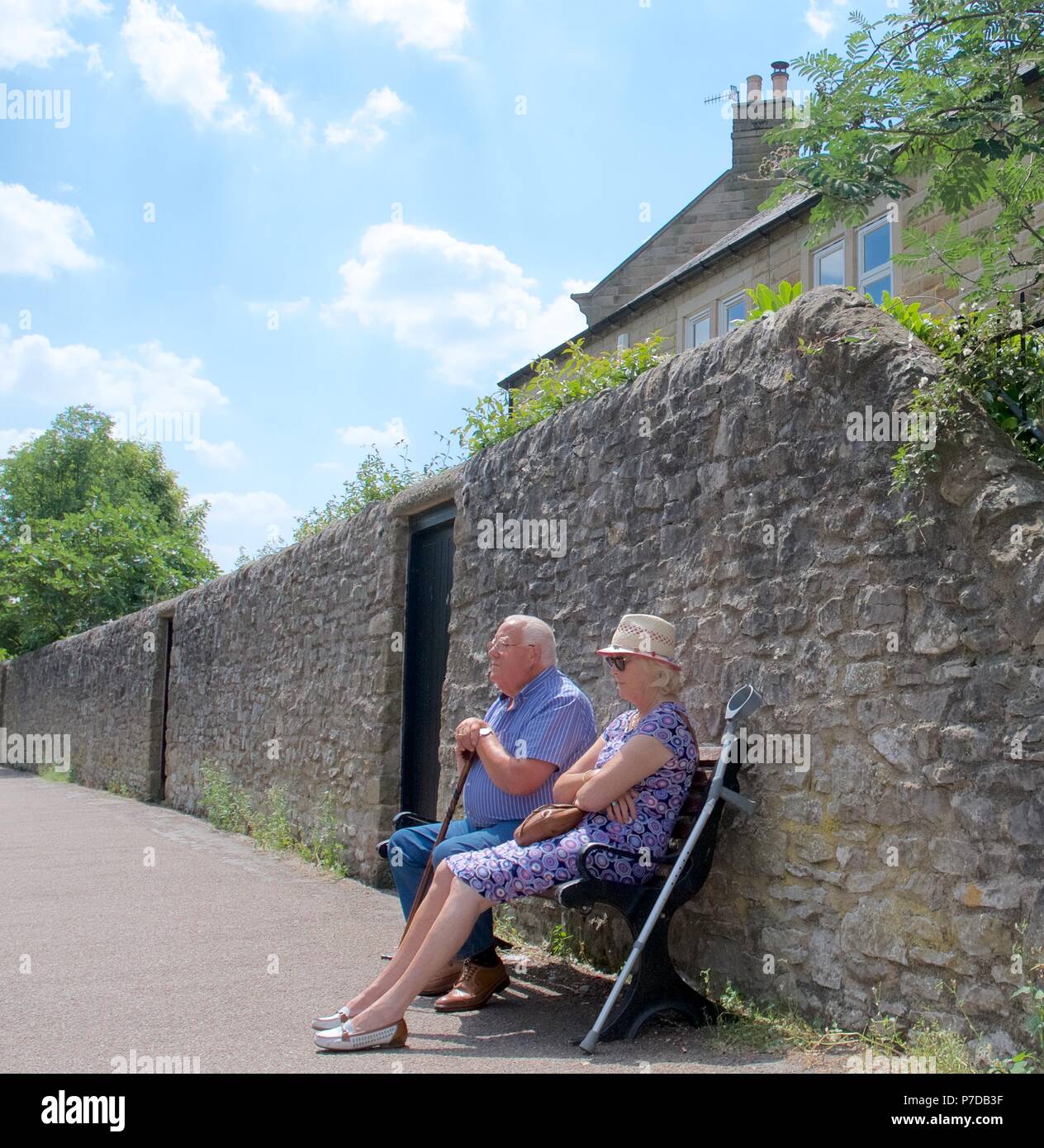 Ein älterer Mann und eine Frau auf einem Sitz an einem heißen Tag in Bakewell, Derbyshire entspannen Stockfoto