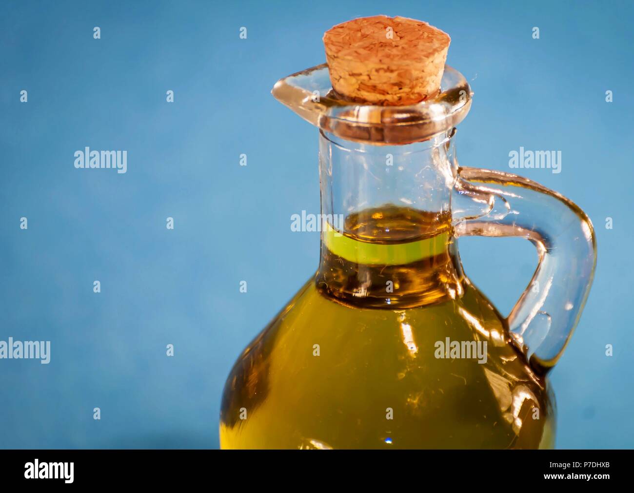 Ein nettes kleines Glas Flasche mit Premium Qualität natives Olivenöl mit einem Korken verschlossen. Öl jar Nahaufnahme mit blauen Hintergrund isoliert. Stockfoto