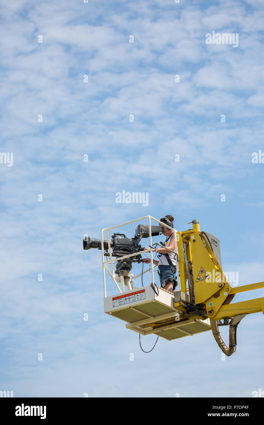 Portraitfotos einzelner Fernsehen Kamerafrau auf erhöhten Plattform angehoben hoch in der Luft Dreharbeiten Sport Event für live übertragen. Blauer Himmel & Wolken. Stockfoto