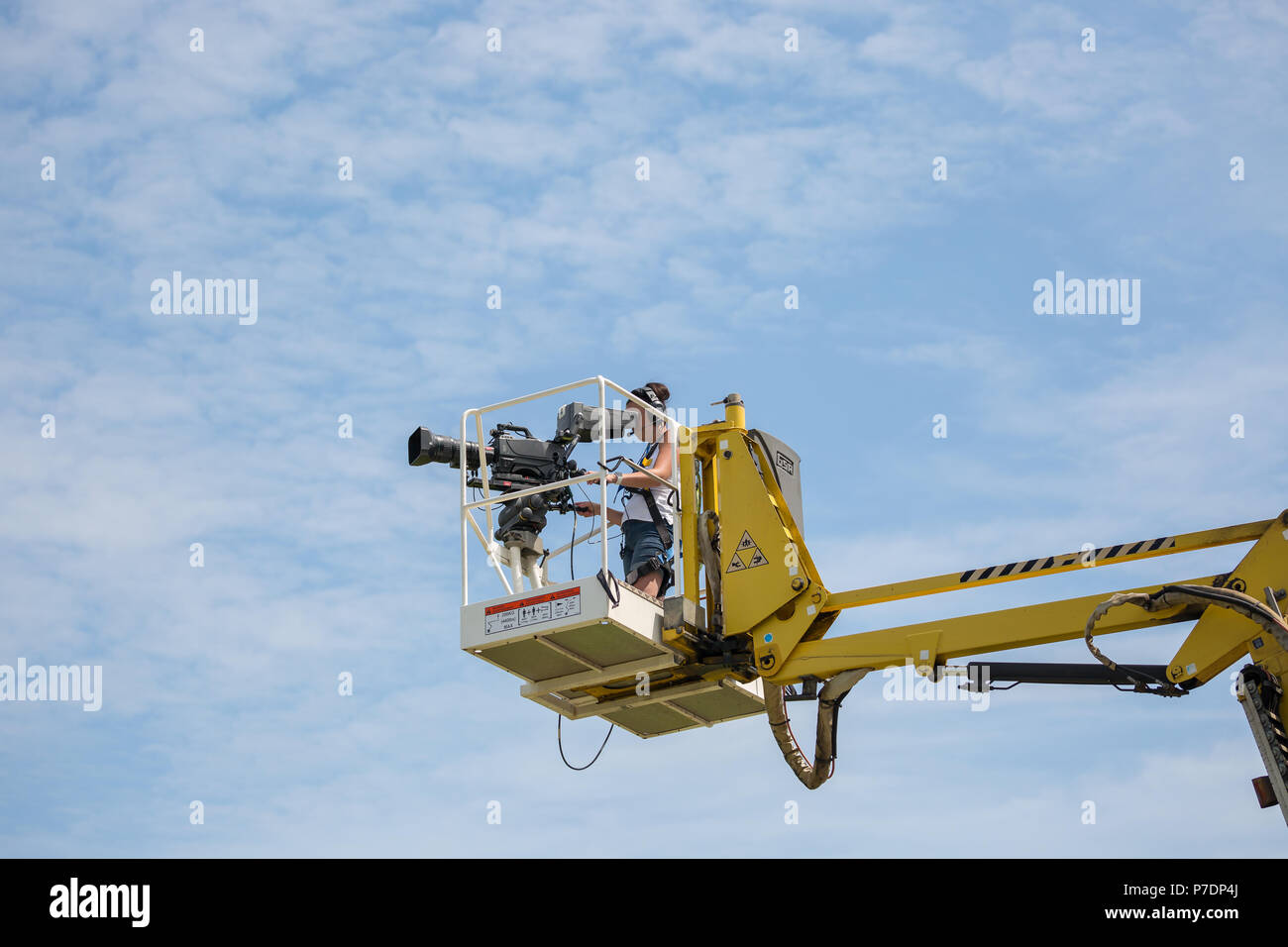 Seitenansicht des einzigen Fernsehen Kamerafrau auf erhöhten Plattform angehoben hoch in der Luft Dreharbeiten Sport Event für live übertragen. Blauer Himmel, wispy Wolken. Stockfoto