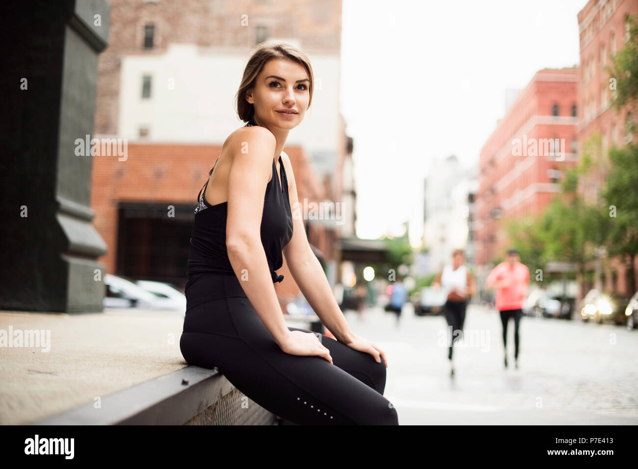 Portrait von Frau sitzt auf der Wand an der Kamera suchen, New York, USA Stockfoto