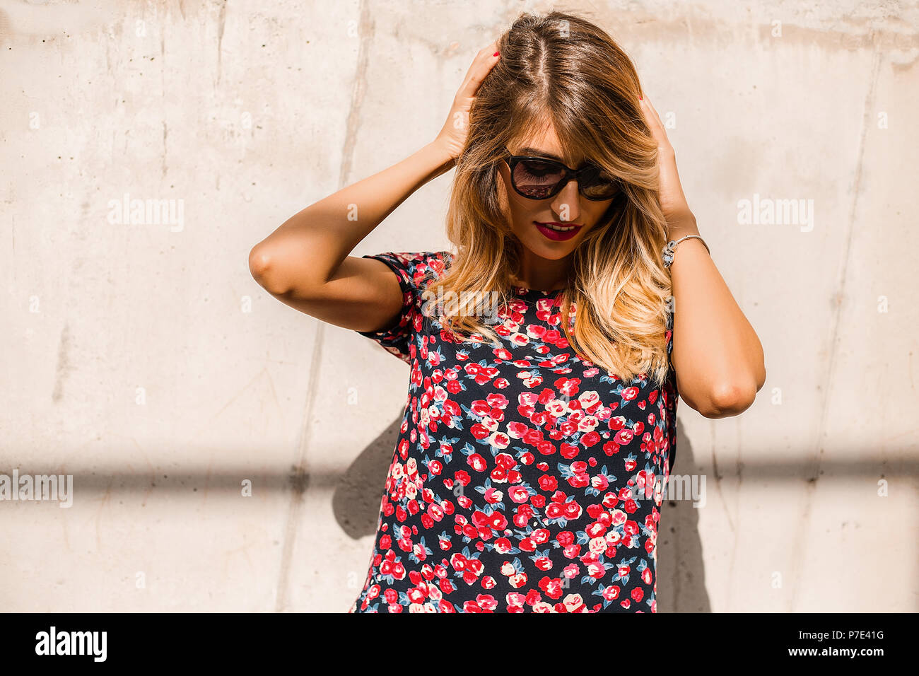 Blond, stilvolle Mitte der erwachsenen Frau Sonnenbrille tragen vor der Wand mit den Händen in das Haar Stockfoto